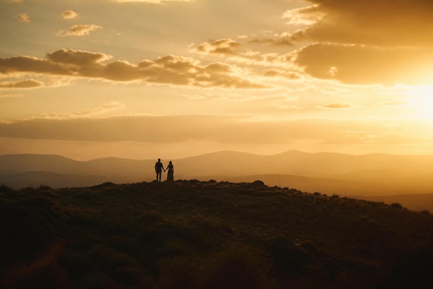 A couple standing together on a ridge at golden sunset
